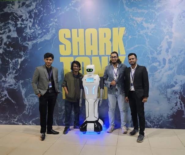 Four Roboway team members with the Pixi humanoid robot in front of a Shark Tank backdrop